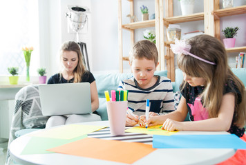 Siblings drawing with colorful pencils together while mother working on laptop