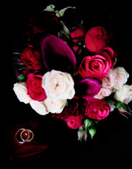 Pink and red wedding bouquet stands over golden rings