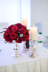 Little rose bouquet stands before burning white candle