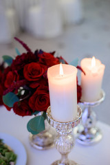 White candles burn before little bouquet of roses