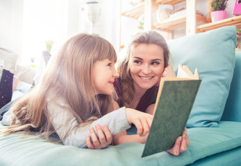 Mother and daughter sitting on sofa and reading book together