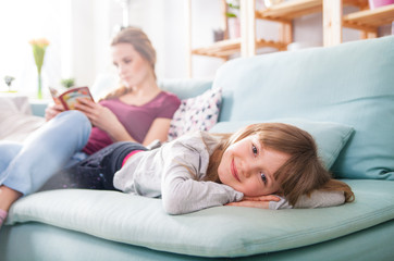 Mother and daughter sitting on sofa and reading book