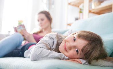 Mother and daughter sitting on sofa and reading book