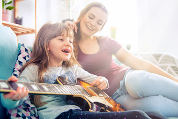 Mother and daughter at home, playing guitar and singing