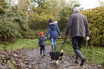 Multi Generation Family Take Dog For Walk In Fall Landscape