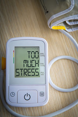 Digital blood pressure meter with warning message TOO MUCH STRESS on the monitor. Health hazard concept