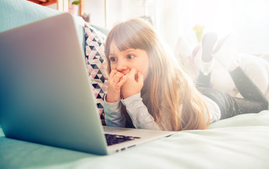 Excited little girl watching movie on laptop at home