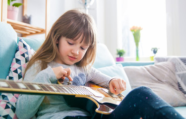 Cute little girl playing guitar at home