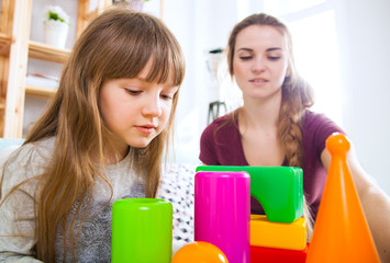 Cute little girl and her mother playing with blocks together, family at home