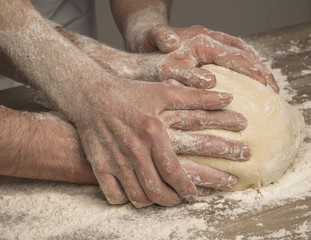 Manos  unidas amasando pan de harina en mesa de madera de forma artesanal