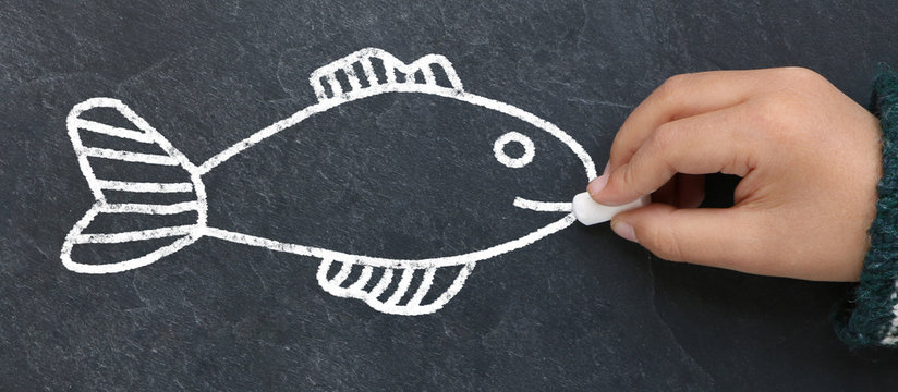 Enfant dessinant un poisson &agrave; la craie sur une ardoise