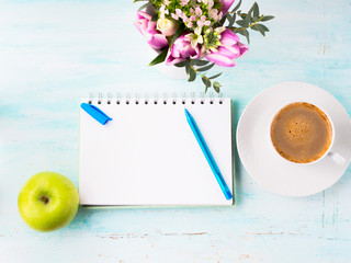 Blank empty notebook page with blue pen and cup of coffee. Spring summer flat lay with flowers and green apple