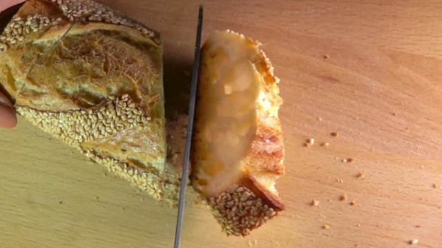View from above on slow motion of knife cutting off a loaf freshly baked baguette