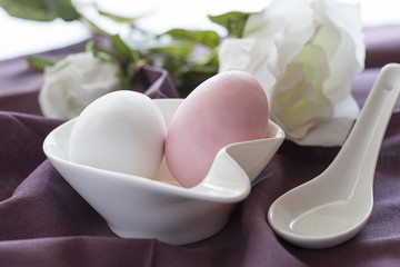 Uova di zucchero rosa e bianco dentro a contenitore bianco e sullo sfondo una rosa bianca