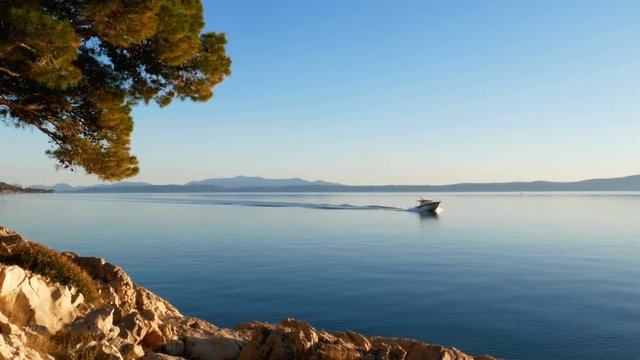 Speed boat passing by scenic coastline of Adriatic sea on sunny day
