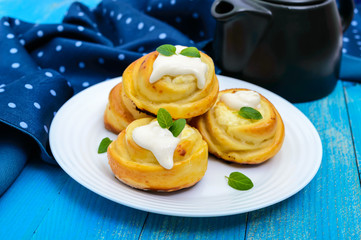 Freshly baked, cottage cheese buns, with cream and mint leaves on a white plate on a blue background.