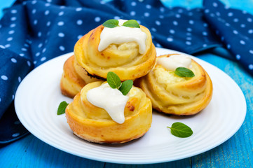 Freshly baked, cottage cheese buns, with cream and mint leaves on a white plate on a blue background.