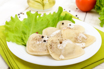 Italian ravioli (dumplings) in the shape of a heart on a plate on white wooden background.