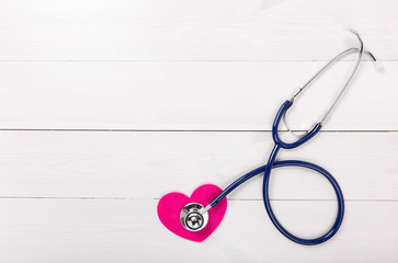 Stethoscope on heart shape over white wooden background