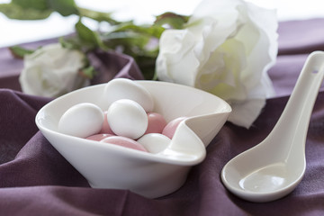 Fototapeta na wymiar Ovetti di zucchero bianchi e rosa dentro a contenitore bianco e sullo sfondo una rosa bianca