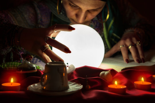 Gypsy fortuneteller gazes into crystalball,using sorcery