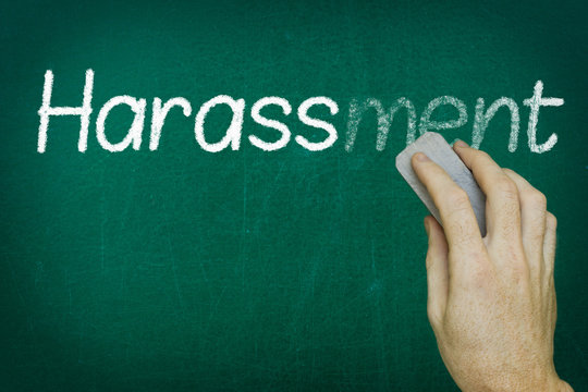 Hand erasing the word HARASSMENT written on blackboard