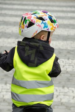 Little child rides a bike across the zebra crossing.  Boy is marked by yellow reflective vest and helmet because of visibility and safety.