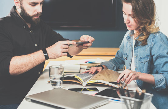 Businesswoman and businessman sitting at table and watch catalog of finishing materials.