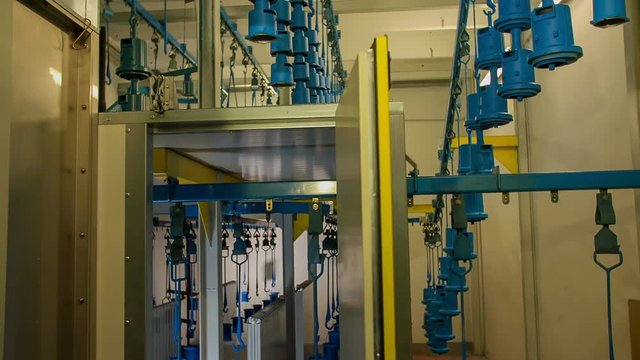 We can see blue items travelling very slowly on a conveyor belt hanging from the ceiling and inside a room. There is an upper and lower level.
