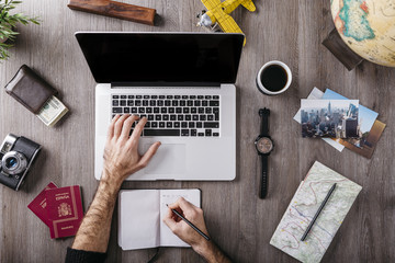 Overhead view of man using laptop surrounded by travel items on table