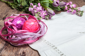 Pinkfarbenes Osternest auf Holztisch mit weißer Tischdecke und Blumenschmuck