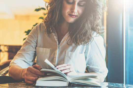 Young businesswoman in white shirt sitting at table and reading book. Girl leafing through book