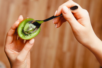 girl with beautiful nails is eating a ripe kiwi with a tea dessert spoon. Demonstration of kiwi...