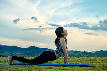 Woman practicing Upward-Facing Dog yoga pose outdoors over sunset sky background.