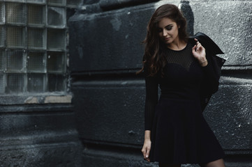 Eastern beautiful woman wearing biker jacket poses in backyard of vintage apartment house