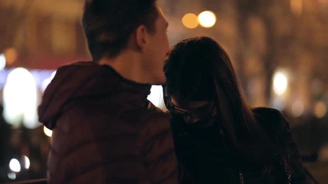Young couple sitting on a bench together in a night street