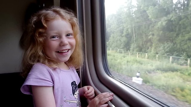 Beautiful little girl laughing in front of the train window while travelling raylway