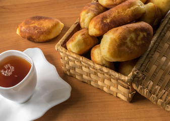 Traditional Homemade Baked Patties or Pies with Jam in a Wicker Basket next to a White Cup of Tea