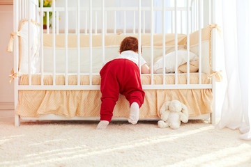 cute toddler baby climbing into the cot in nursery room at home