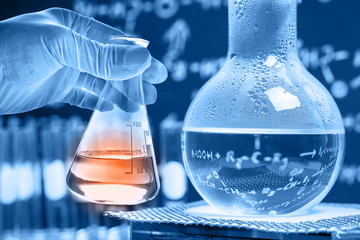 Flask in scientist hand with test tubes in laboratory  