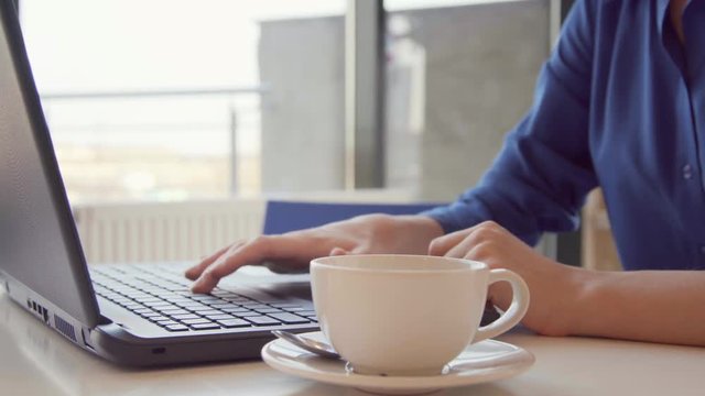 Young woman having a coffee break, she is stirring her espresso and using a laptop, hand close up, seamless loop.