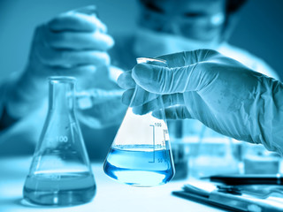 Flask in scientist hand with blur scientist in laboratory