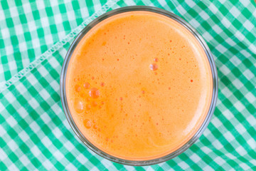 Fresh carrot juice in glass on napkin, close-up, top view.