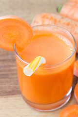 Fresh carrot juice in glass with straw and carrot vegetable on wooden table.