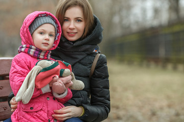 Happy young mother and child daughter hugging sitting on bench in spring park