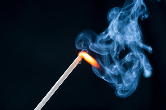 Burning match in smoke on black background