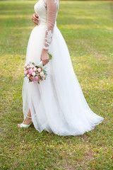 the bride holds in hand the bouquet from pink peonies outdoors on a green lawn. Wedding day