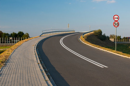 Wiadukt z asfaltową nawierzchnią przechodzący nad autostradą z oznakowaniem pionowym i poziomym