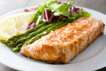 Grilled salmon fillet with asparagus and salad in plate on wooden table

