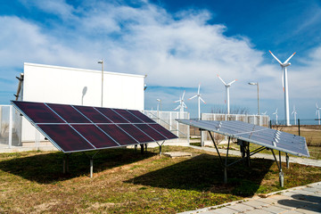 Solar panels in power station against wind turbines background - concept of sustainable resources